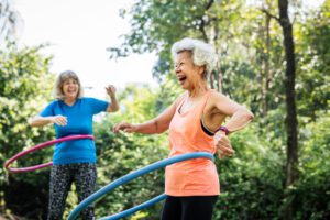 Two smiling women use hula hoops to stay active and have fun.